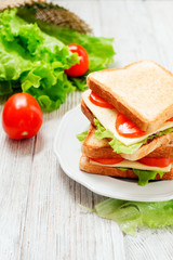 
breakfast or lunch , sandwiches with cheese , sausage , tomato, lettuce and mayonnaise on a wooden background