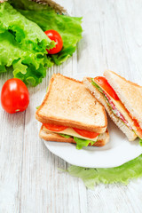 
breakfast or lunch , sandwiches with cheese , sausage , tomato, lettuce and mayonnaise on a wooden background