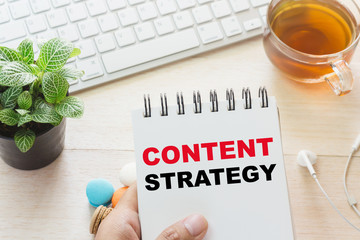 Man holding CONTENT STRATEGY message on book and keyboard with a hot cup of tea, macaroon on the...