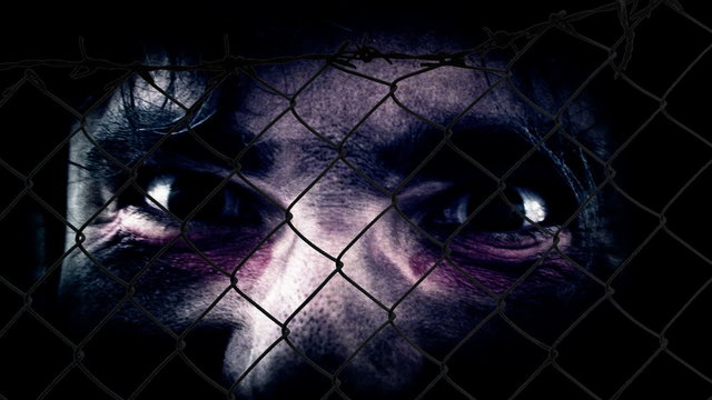 Crazy eyes looking around and in camera, seen through a fence. Spooky Halloween . It can be a zombie, a demon, a ghost, or simply a freak.