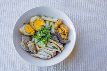 Chinese roll noodle soup with slice pork and  tofu, vegetables in a white ceramic bowl.
tradition food of thailand