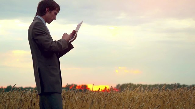 Businessman standing on a wheat field using a tablet. 1920x1080