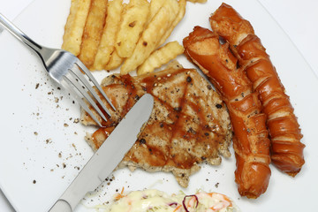 Pork steak and sausage with French fries on white dish.