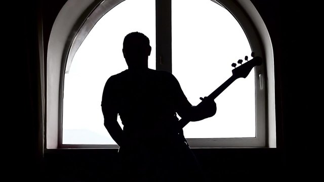 A silhouette of a bass guitar player