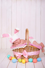 Fototapeta na wymiar Newborn baby girl in a rabbit costume has sweet dreams on the wicker basket. Easter Holiday