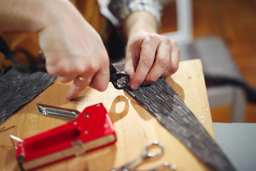 Removing ticks nail out of the board. Man upholstering chair in his workshop