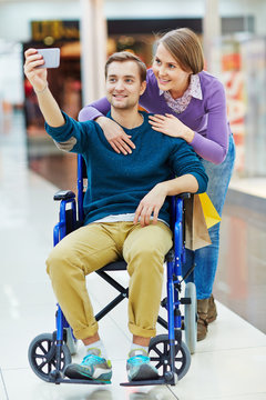 Pretty girl and her boyfriend in wheelchair making selfie during shopping