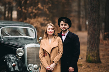 Gorgeous newlywed bride and groom posing in pine forest near retro car in their wedding day