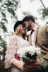 Gorgeous newlywed bride and groom posing in pine forest near retro car in their wedding day
