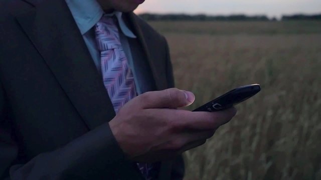 Farmer, businessman, standing in field in twilight and uses mobile phone in slowmotion. 1920x1080