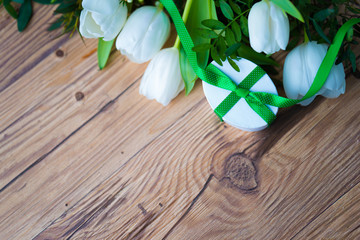 White tulips and a small gift and greenery on wooden board