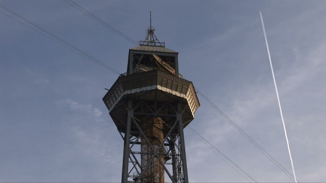Tower of the port cable car in Barcelona, Spain as a plane flies overhead 