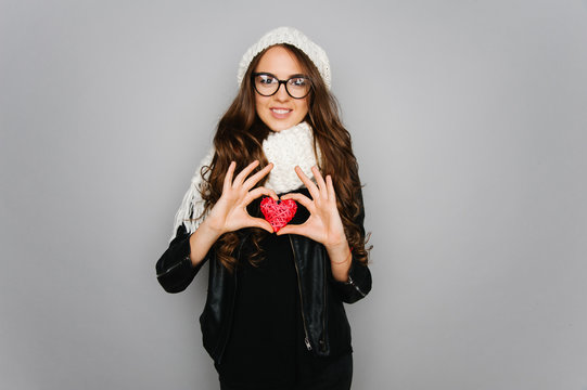 Portrait of cute teen girl with heart in her hand isolated on gray studio background posing to the camera 

