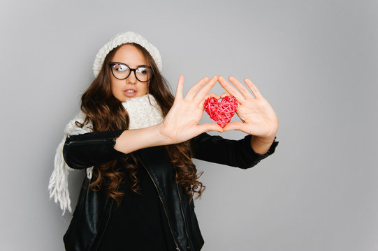 Portrait of cute teen girl with heart in her hand isolated on gray studio background posing to the camera 
