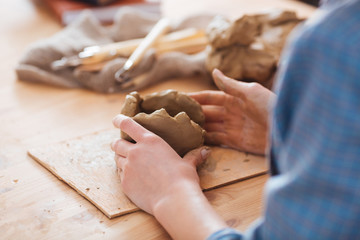 Woman ceramist hands working on sculpture at wooden table