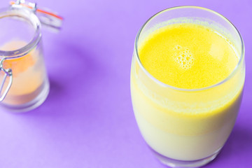 Healthy Drink Made from Turmeric Roots, Exotic Spices with Coconut Milk, Honey, Lemon and Ghee on Purple Background, Close-up