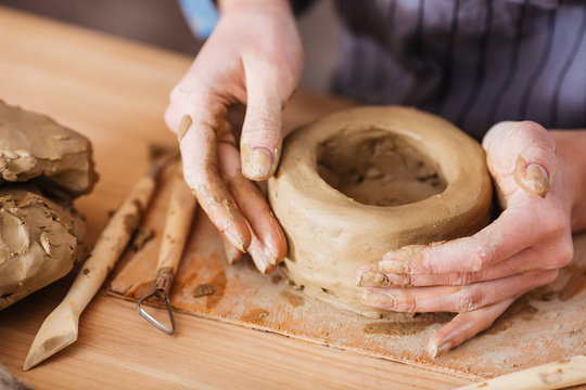 Hands of young woman making earthen pot on wooden table