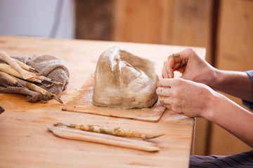Hands of woman ceramist finishing sculpture with clay in workshop
