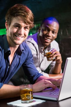 Two men having whiskey and using laptop at bar counter