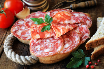 Spanish tapas - sliced salame on rustic wooden cutting board with bread and tomatoes