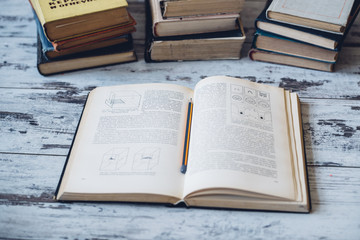 Piles of old textbooks with one book in front open and pencil lying on its pages