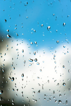 Raindrops on window glass with bright  blue cloudy sky background