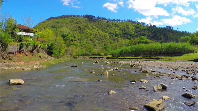 Beautiful view of river flows near village with green forest on the hill under sky with white clouds, Georgia, Guria