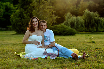 Happy pregnant couple sitting on the grass in park