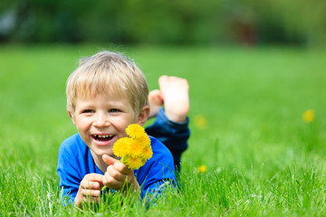 cute happy little boy lying in green grass on spring
