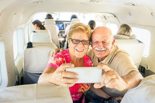 Senior happy couple taking selfie with mobile phone on board of plane  -  Smiling retired people having fun flying from Coron to Borakay  - Concept of elderly happiness on world wide travel 