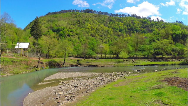Beautiful view of river flows near village with green forest on the hill under sky with white clouds, Georgia, Guria