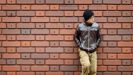 Fototapeta na wymiar An Asian Man in a Brown Jacket Leans Against the Wall