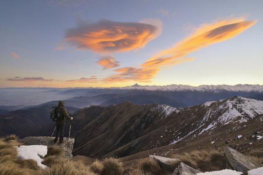 Hiker with backpacking observes the Alps under a spectacular sky with lenticular clouds.