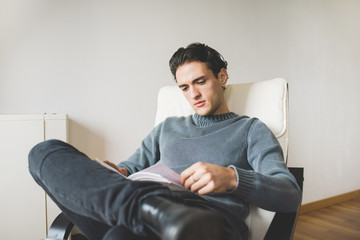 Young handsome caucasian man sitting on the armchair in his hous