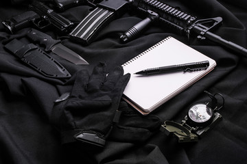 Workplace for the soldier with clean notebook for writing.Top view/Workplace for the soldier: notebook with pen, gloves,knife and pistol, rifle and compass on black fabric