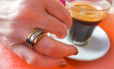 Ring on her finger, espresso in a cup.  A woman wearing a puzzle ring about to raise her cup of espresso.