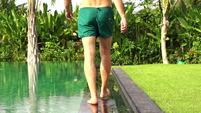 Handsome man walking along edge of swimming pool 
