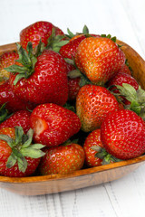 Fresh organic strawberries in bowl on white wooden background