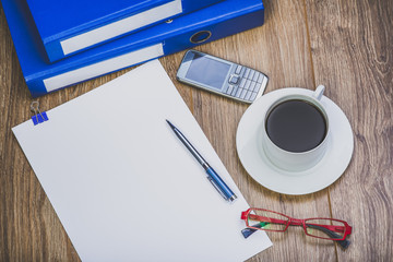 View Of An Office Desk With Ring Binders, Cell Phone, Coffee Cup, Sheet Of Paper, Glasses And Pen. Office Desk In Retro Style.