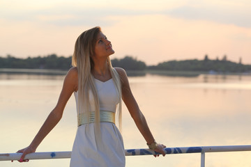 pretty dressed young girl looking up at a lake at sunset