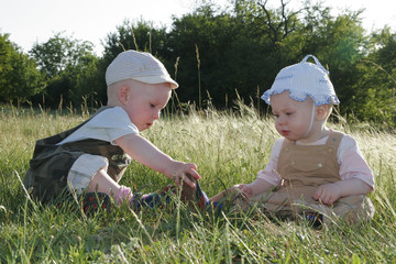 Two children are sitting quietly on a sunny meadow and communicate