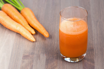 Healthy carrot juice in a glass and raw carrots on a wooden background. Shallow dof