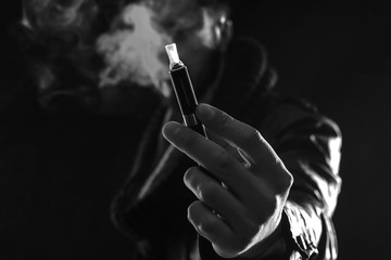 Hand holding an electronic cigarette over a dark background black and white - obrazy, fototapety, plakaty