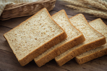 Whole wheat bread slices and wheat on wooden table