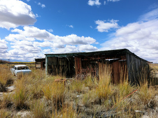 Fototapeta na wymiar Abandoned wooden prairie shack with old car - landscape color photo