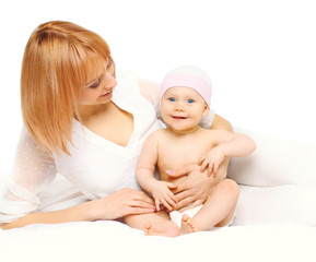 Happy mother with baby lying together on bed over white backgrou