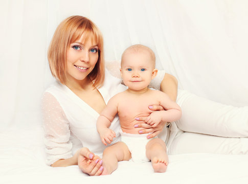 Happy smiling mother with baby lying together on bed at home