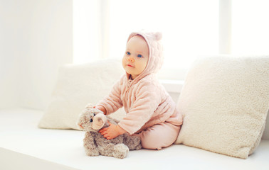 Cute baby playing with teddy bear toy at home in white room near