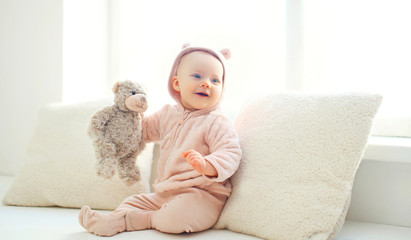 Happy cute smiling baby with teddy bear toy at home in white roo