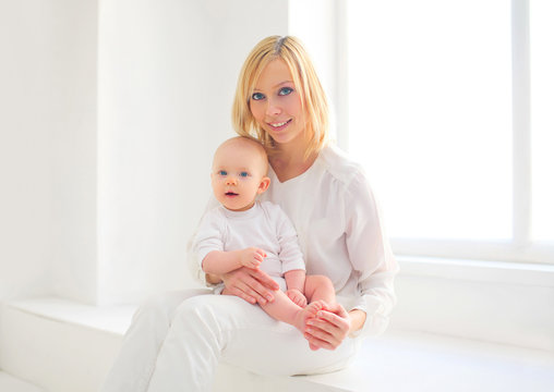 Happy smiling mother and baby home in white room near window